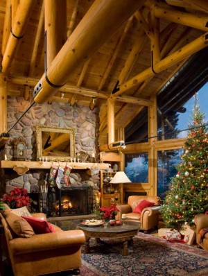 The original builder cut the chord of the open-beam truss system and inserted black steel tie rods to keep the log from interrupting the view through the expansive living room windows. log home beams stone fireplace great room christmas tree